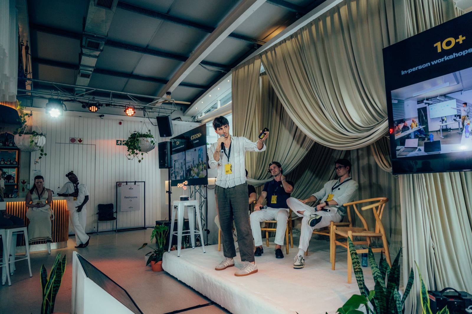 Riccardo Belli sul palco di un evento, sugli schermi i numeri "10+ in-person workshops" e "€300k+".